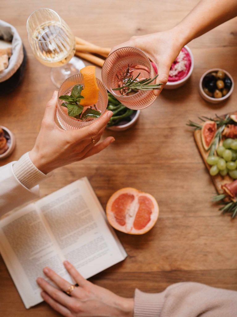 Zwei Hände stoßen mit Drinks über einem aufgeschlagenen Buch an